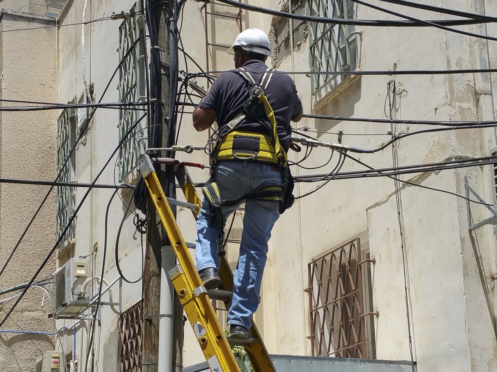Operario con casco y arnés conectando cables eléctricos en la fachada de un edificio