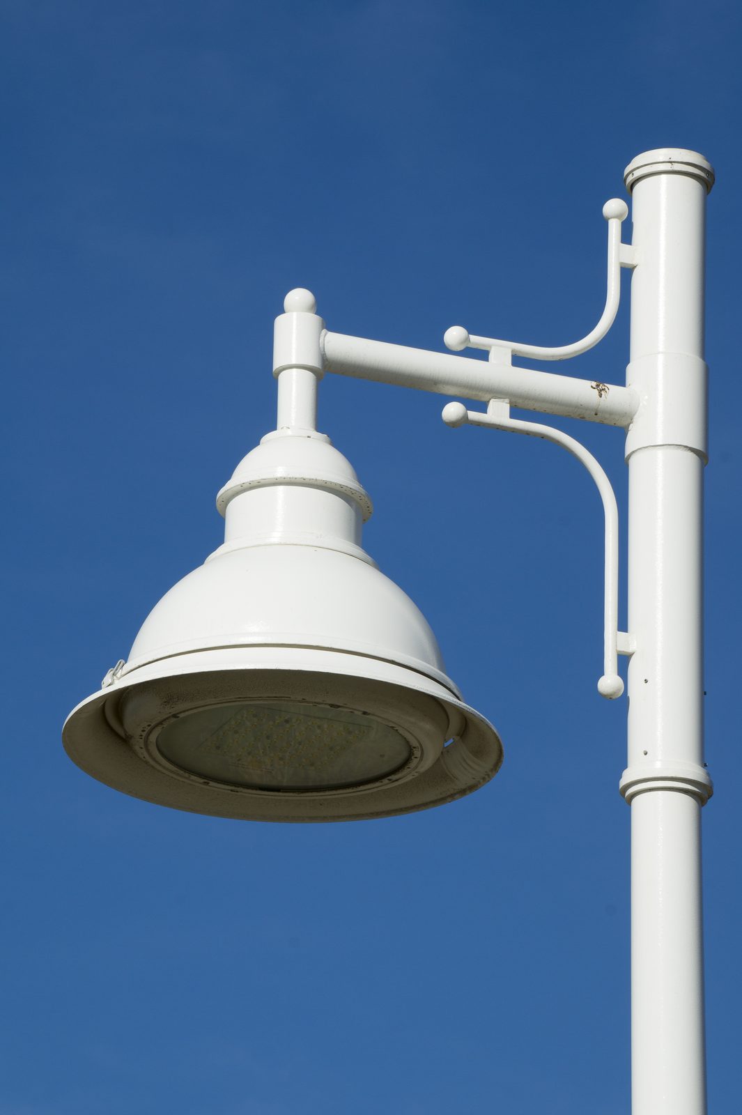Farola LED de alumbrado público blanca con panel de diodos visible sobre cielo azul