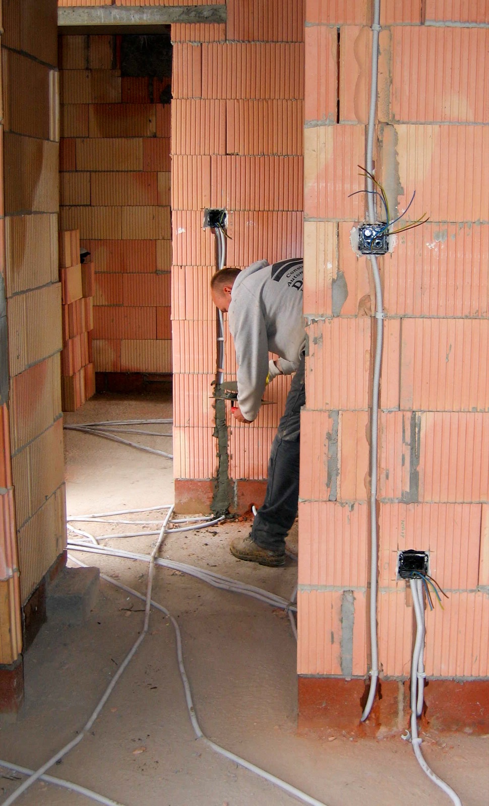 Electricista trabajando en una vivienda en obra con tubos para cableado eléctrico recorriendo las paredes de ladrillo hasta las cajas de mecanismos
