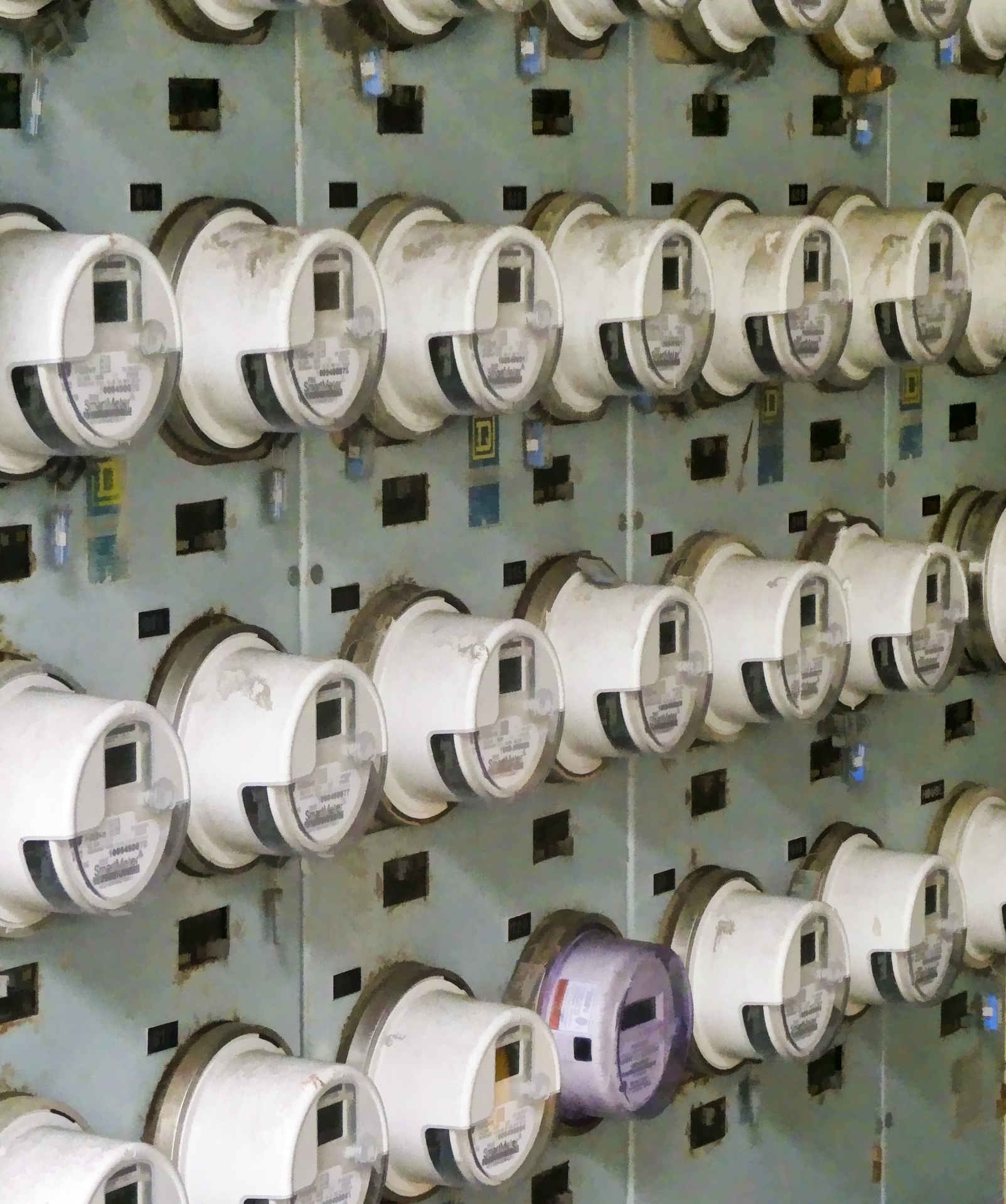 Batería de contadores de electricidad agrupados en filas sobre un panel metálico de un edificio