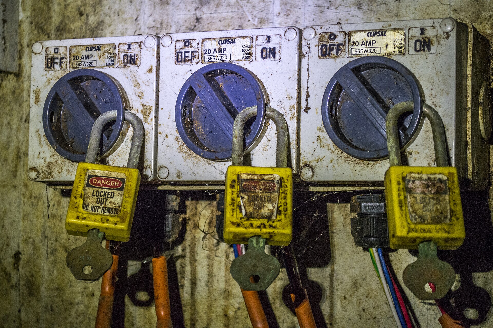 Tres interruptores seccionadores industriales en posición OFF bloqueados con candados amarillos de seguridad con la etiqueta Danger Locked Out