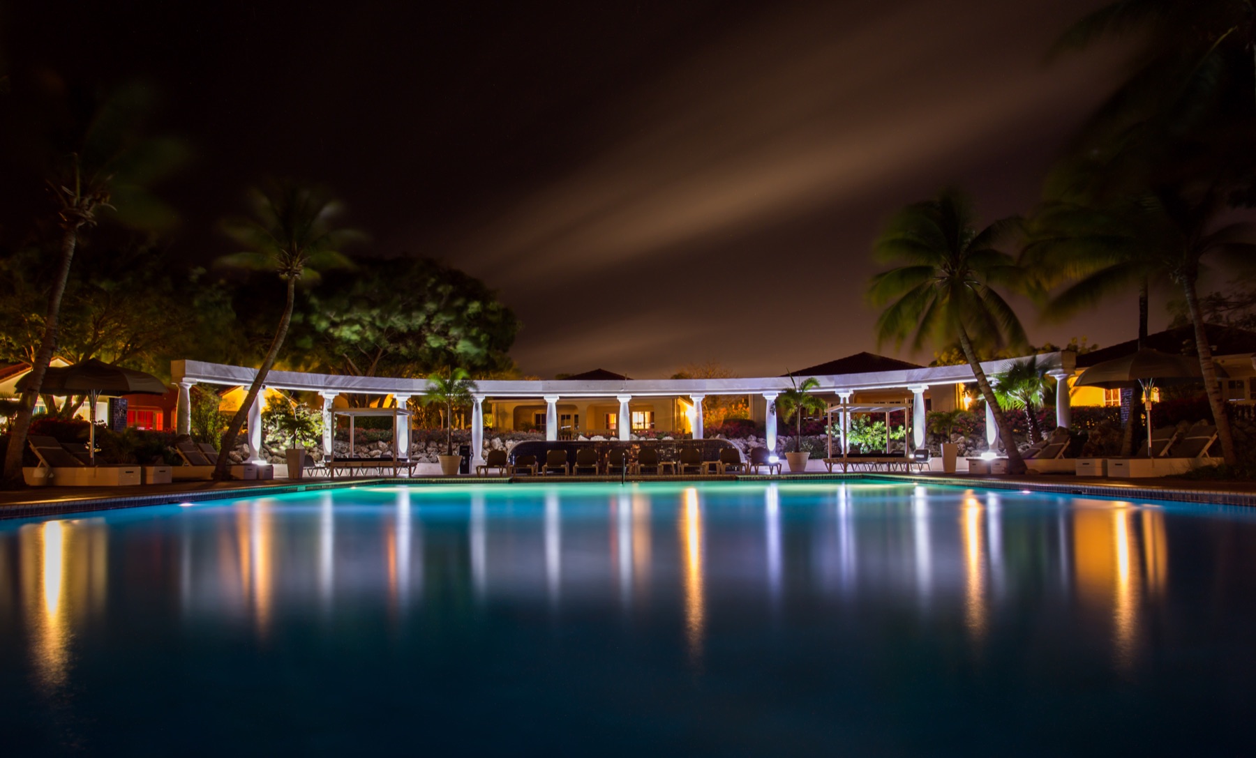 Piscina iluminada de noche con focos sumergidos reflejados en el agua