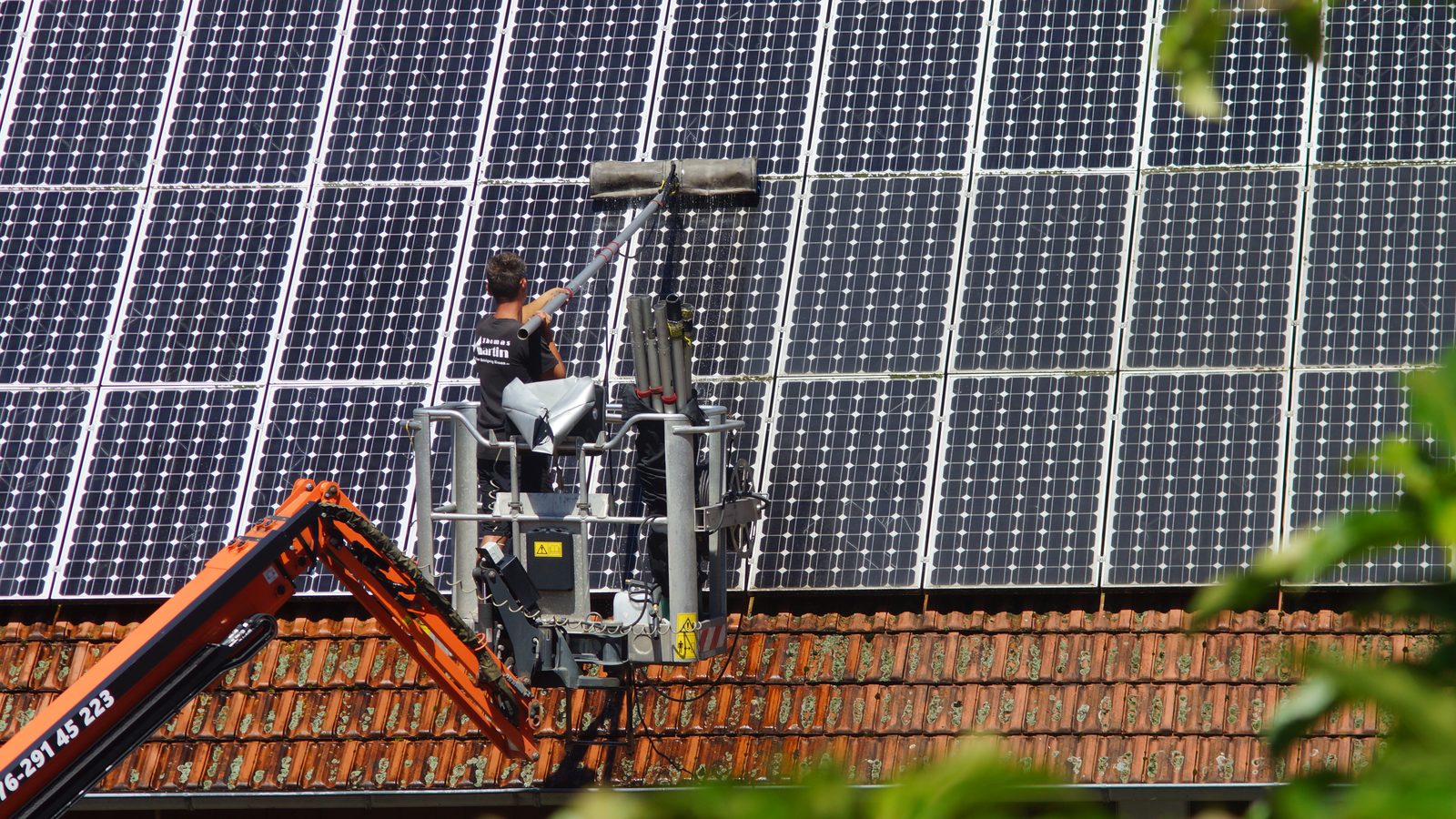 Operario limpiando con un cepillo suave la superficie de unos paneles solares fotovoltaicos