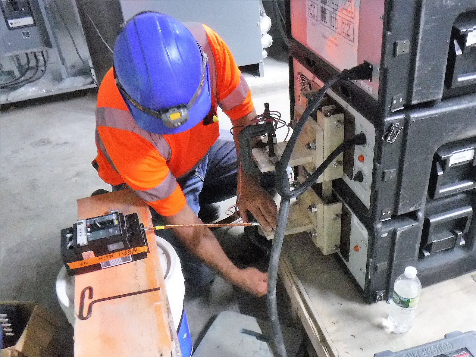 Técnico con casco conectando las pinzas de un equipo de ensayo a un interruptor automático industrial durante una prueba de aislamiento